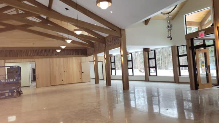 Spacious, modern room with wooden beams, large windows, glass door, and polished concrete floor.
