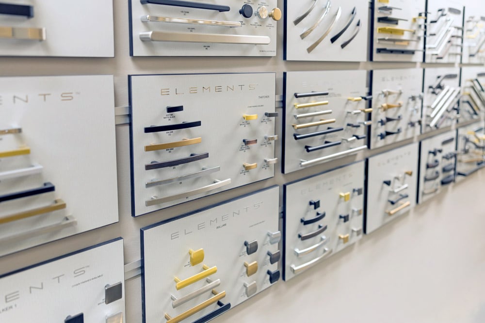 Display boards featuring various styles and finishes of cabinet handles and drawer pulls on a wall.