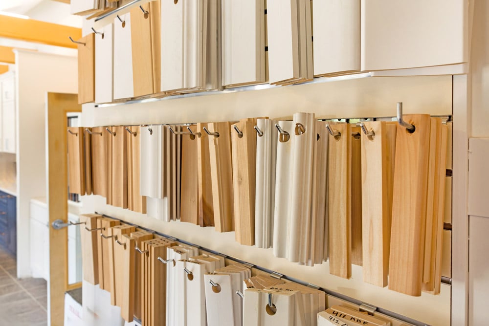 Samples of wood and laminate cabinet door fronts are displayed hanging on metal rods in a showroom.