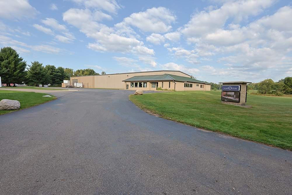 A tan industrial building with a green roof sits by a paved driveway and grassy lawn under a partly cloudy sky.