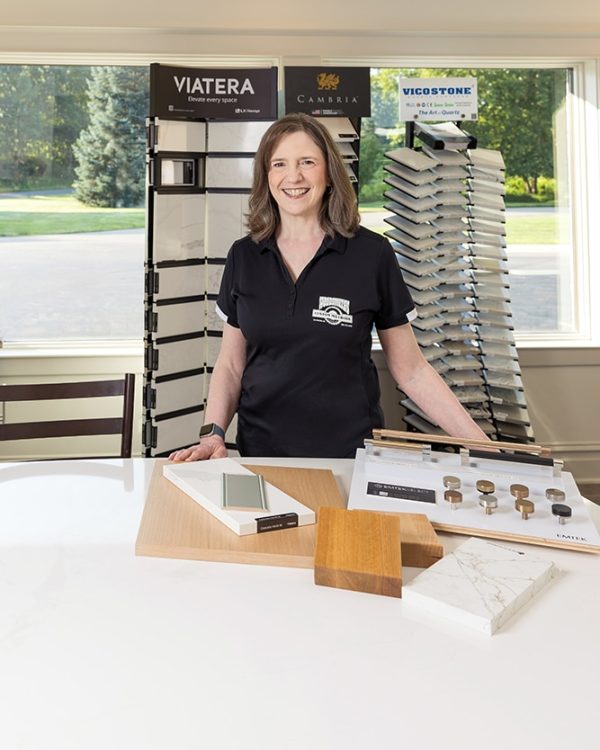A smiling woman stands at a counter with countertop and hardware samples in a bright showroom.